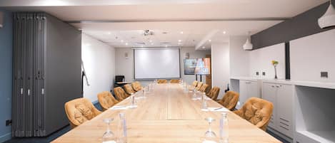 Una sala de conferencias con una larga mesa, sillas, una pantalla de proyector y una pizarra.
