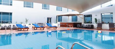 A swimming pool with lounge chairs and umbrellas, surrounded by a building with large windows.