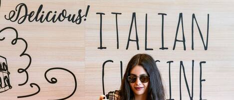 A wooden wall with 'ITALIAN' and 'Delicious!' written on it, and a person holding a slice of pizza.