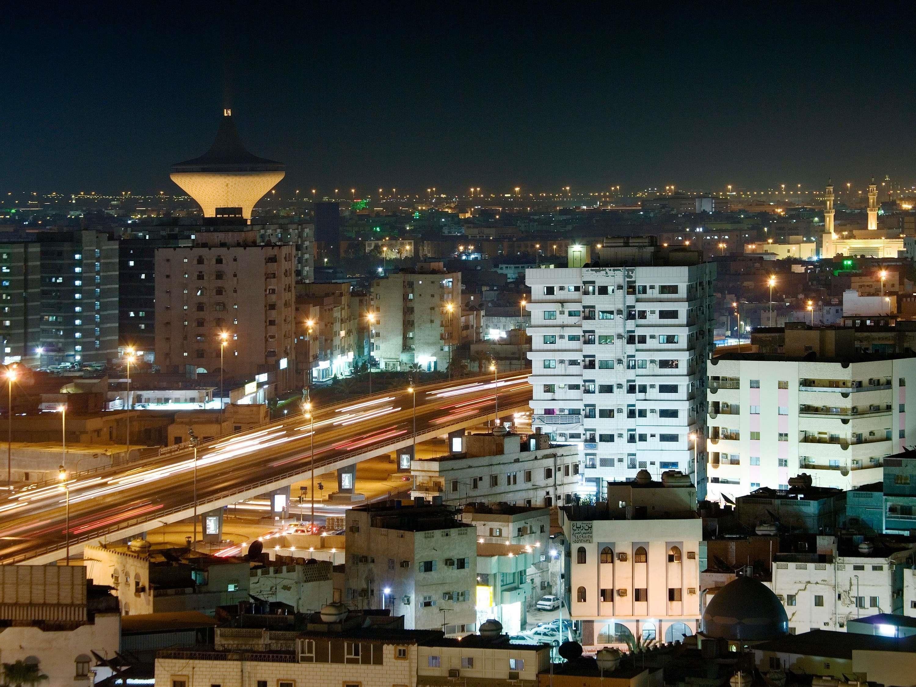 A cityscape at night with illuminated buildings, a prominent tower, and a busy highway.