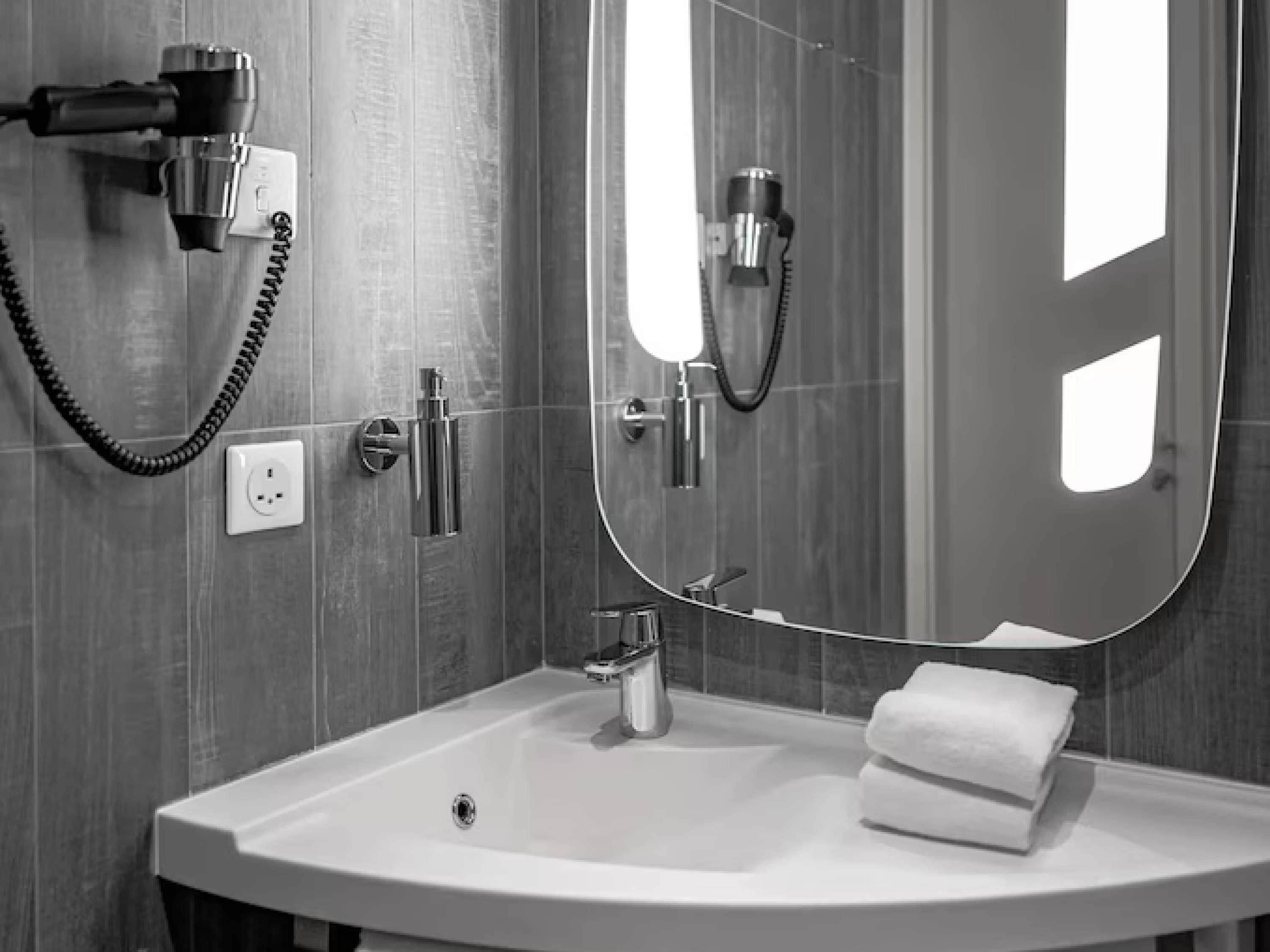 A modern bathroom with a large mirror, a sink, a hairdryer, and a towel.