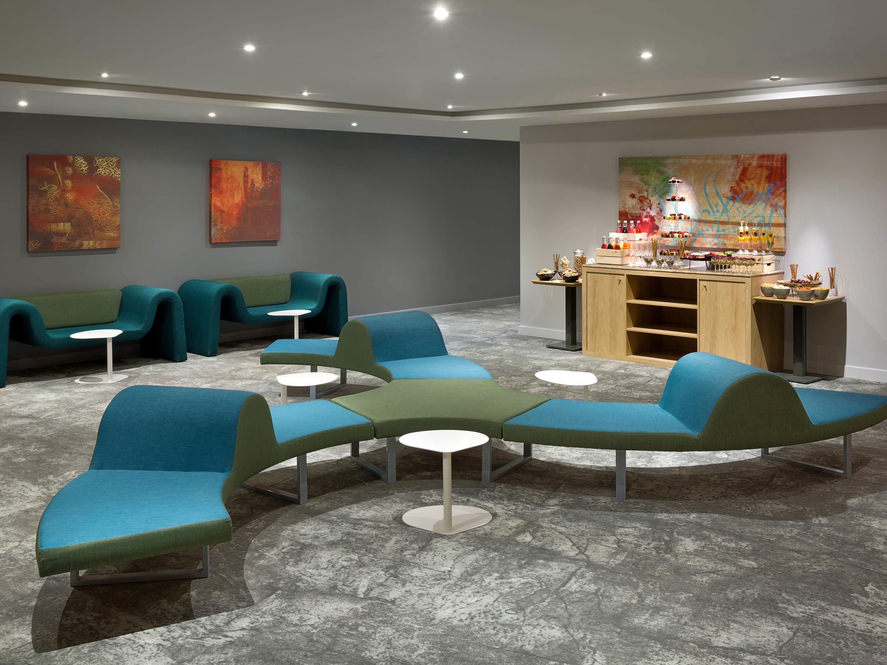 A modern lounge area with curved sofas and small tables, a bar with various items, and abstract art on the walls.