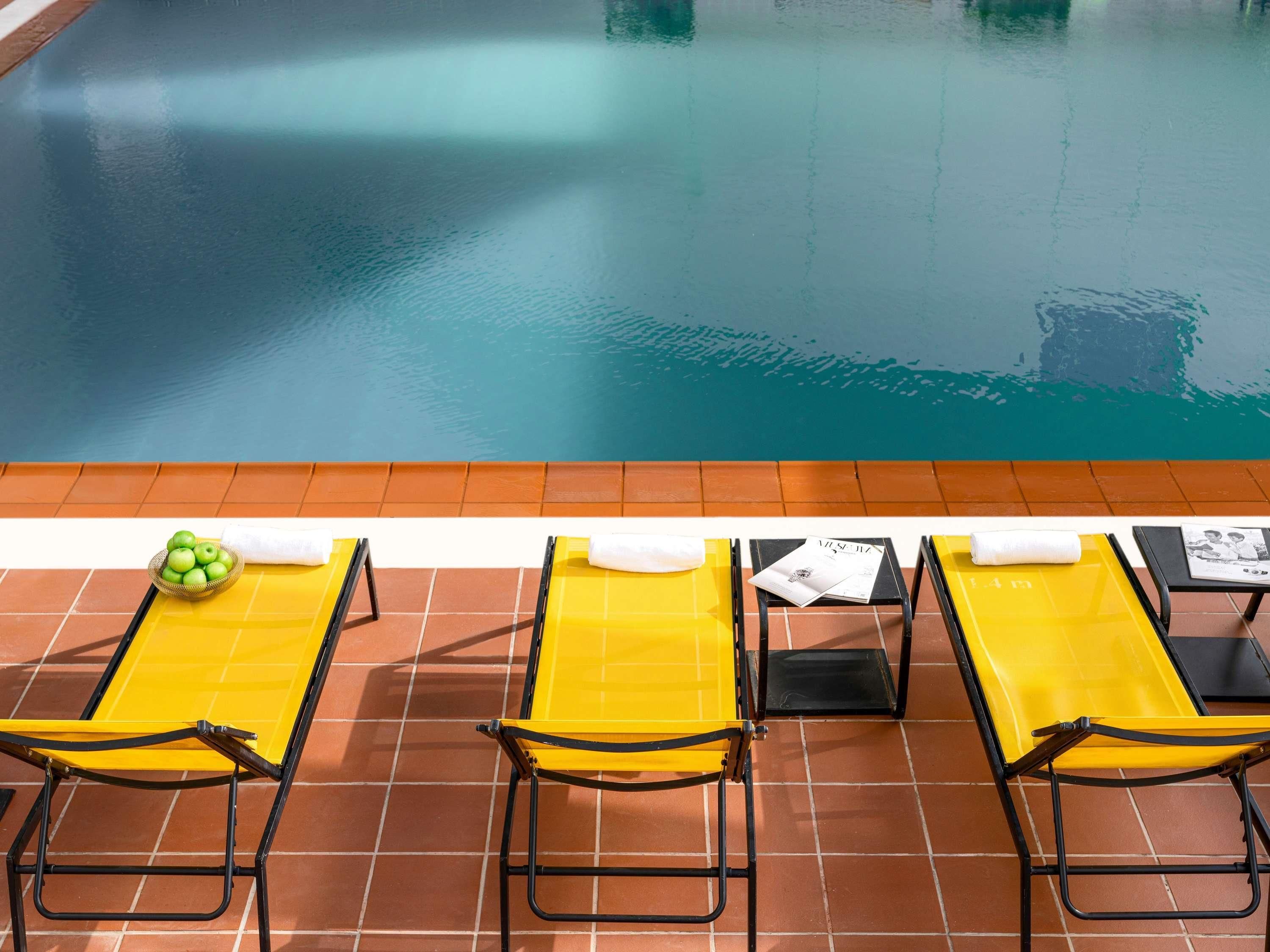 Zona de piscina con sillones amarillos y un bol de manzanas verdes.