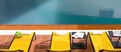 Zona de piscina con sillones amarillos y un bol de manzanas verdes.