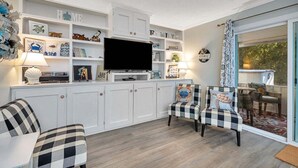 Ein modernes Wohnzimmer mit weißen Schränken, einem Flachbildfernseher und zwei karierten Sesseln.