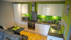 Cocina compacta con muebles blancos, horno integrado, lavamanos y comedor con mesa y sillas.