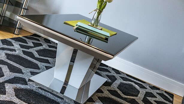 Una mesa moderna con un jarrón de flores blancas, un libro verde y un libro azul sobre una superficie reflectante.
