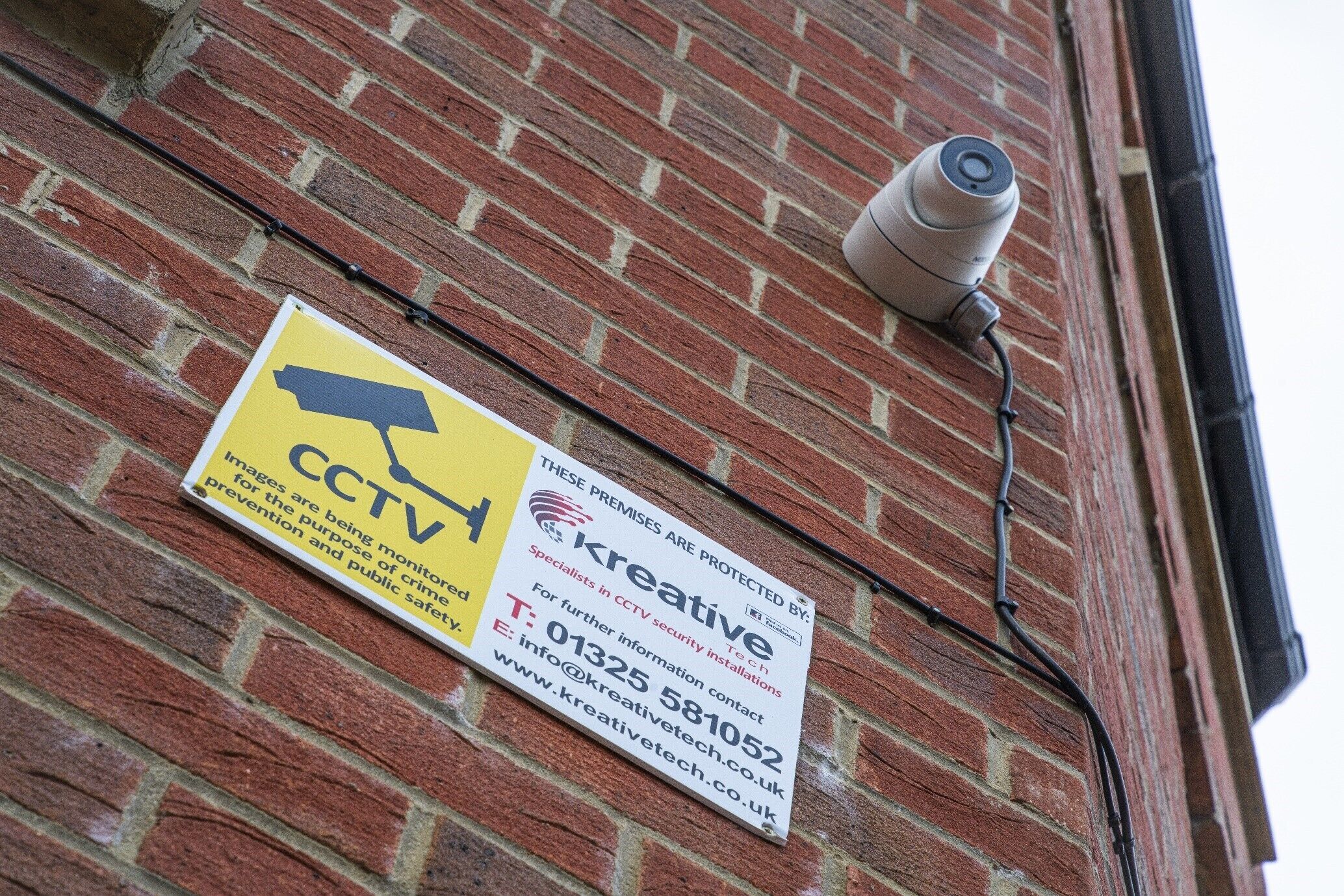 Un mur de briques avec une caméra de vidéosurveillance et un panneau d’avertissement de sécurité.