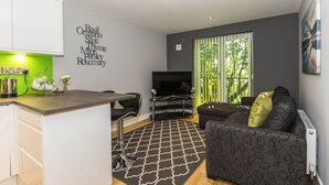Una sala de estar moderna con área de cocina, un sofá, un televisor y una ventana con vista a árboles.