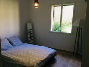Et soveværelse med seng, et vindue, en gulvlampe og en bogreol.