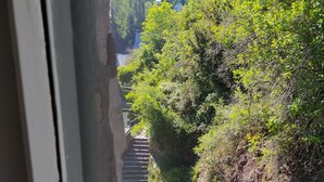 Une vue depuis une fenêtre donnant sur un escalier qui descend le long d’un sentier rocheux, le tout étant entouré de verdure.