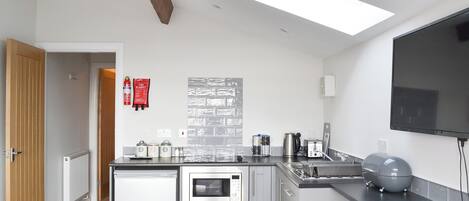 A modern kitchen with a built-in dishwasher, a microwave, and a coffee maker. There is a fire extinguisher on the wall and a flat-screen TV mounted above the counter.