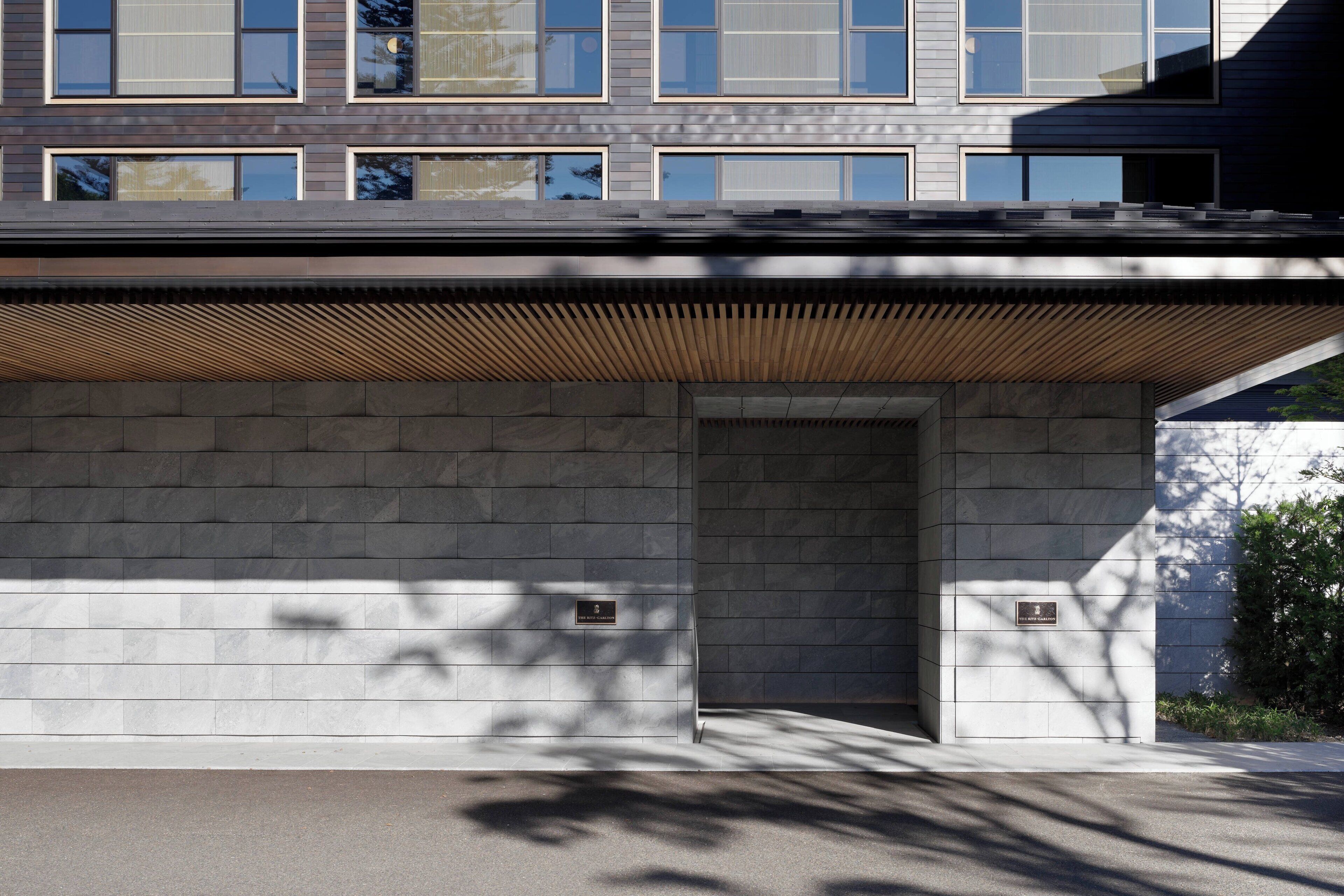 A modern building facade with a flat roof, large windows, and a wooden slatted overhang.