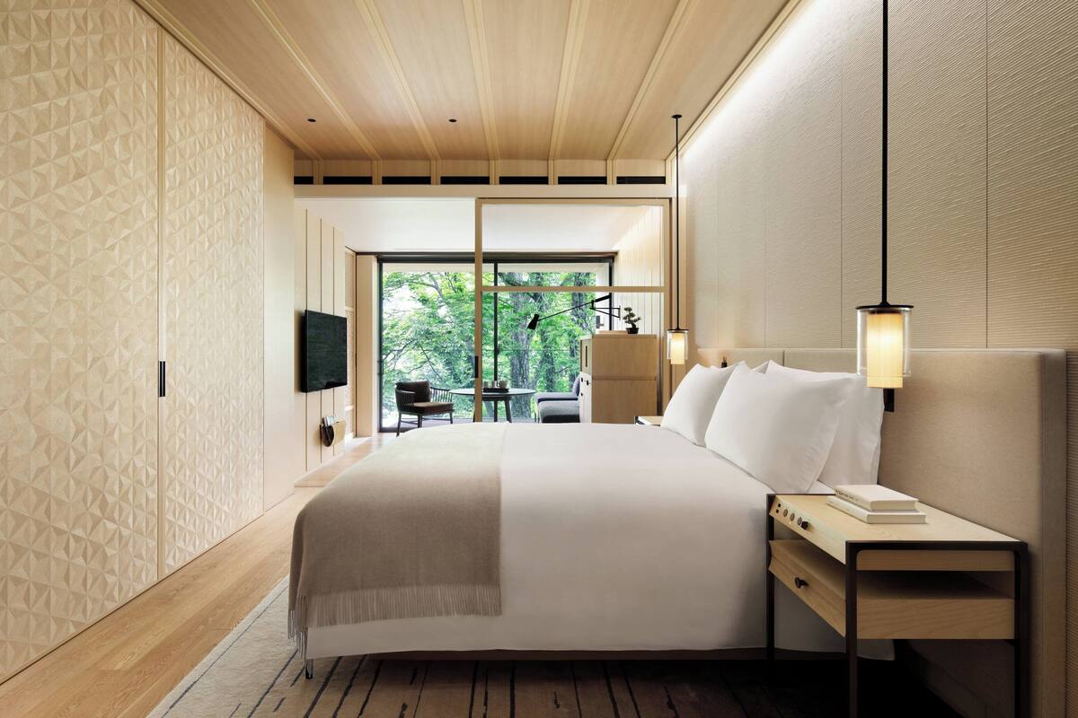 Una habitación de hotel moderna con una cama grande, una mesita de noche con lámpara, un televisor y vistas al exterior.
