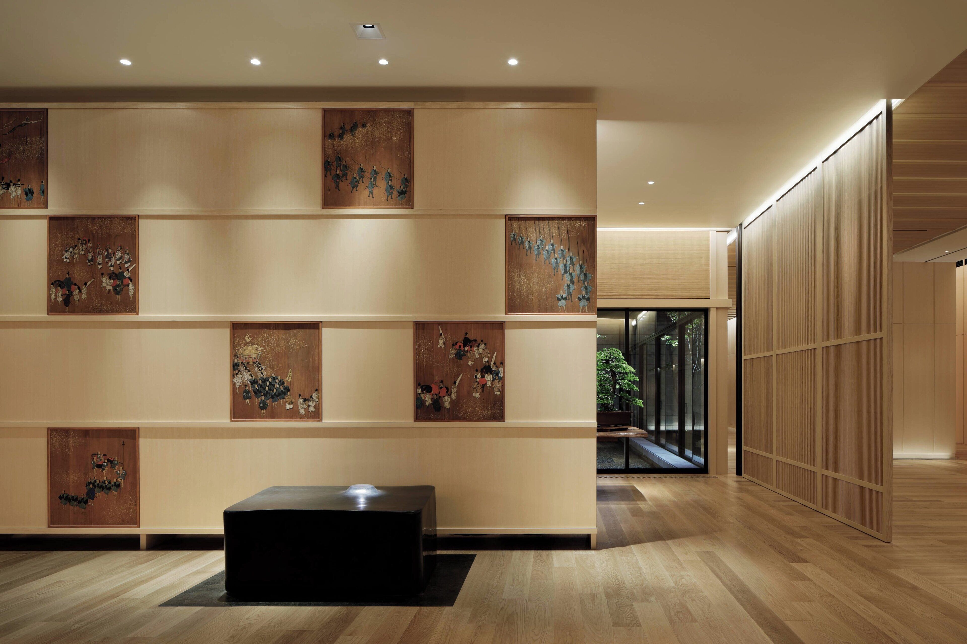 A modern lobby with wooden flooring, a black bench, and artwork on the walls.