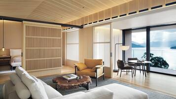 A modern living room with a sofa, armchair, and coffee table. There is a view of a lake through large windows.