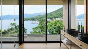 Un baño moderno con un ventanal grande que ofrece una vista panorámica de un lago y montañas.
