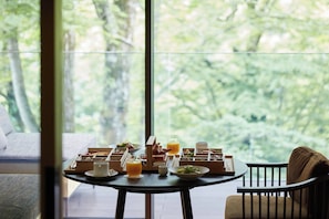 A breakfast setup with a table, chairs, and a view of trees through a large window.