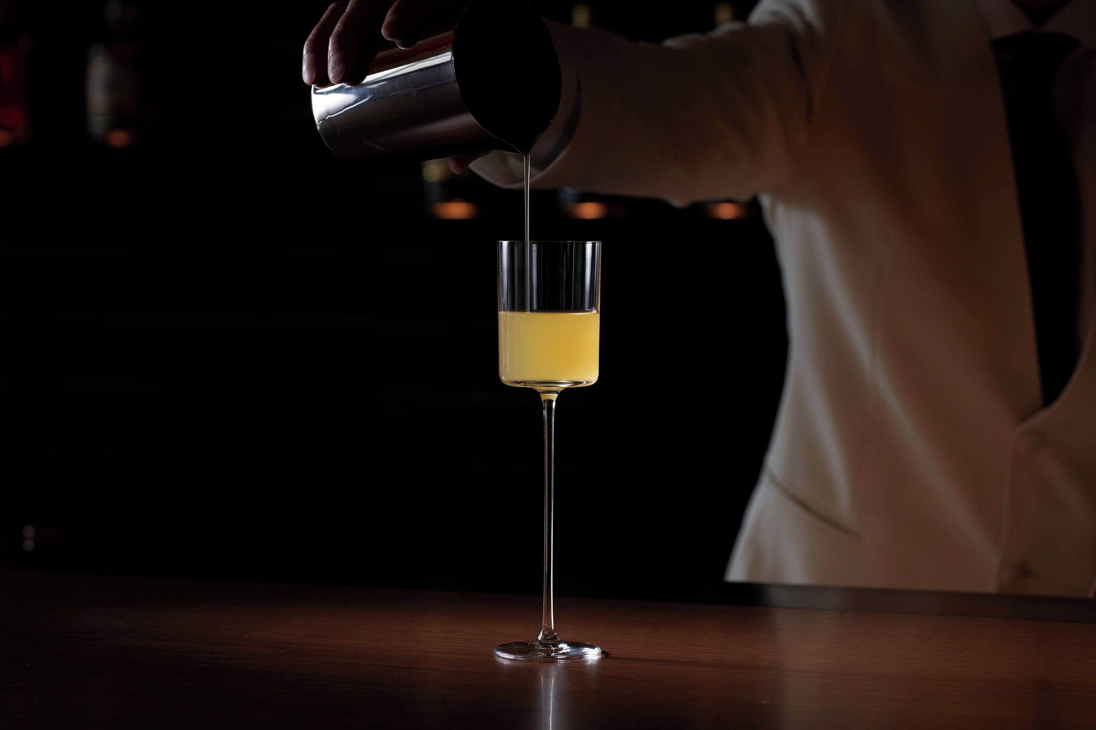 A bartender pouring a drink into a tall glass.