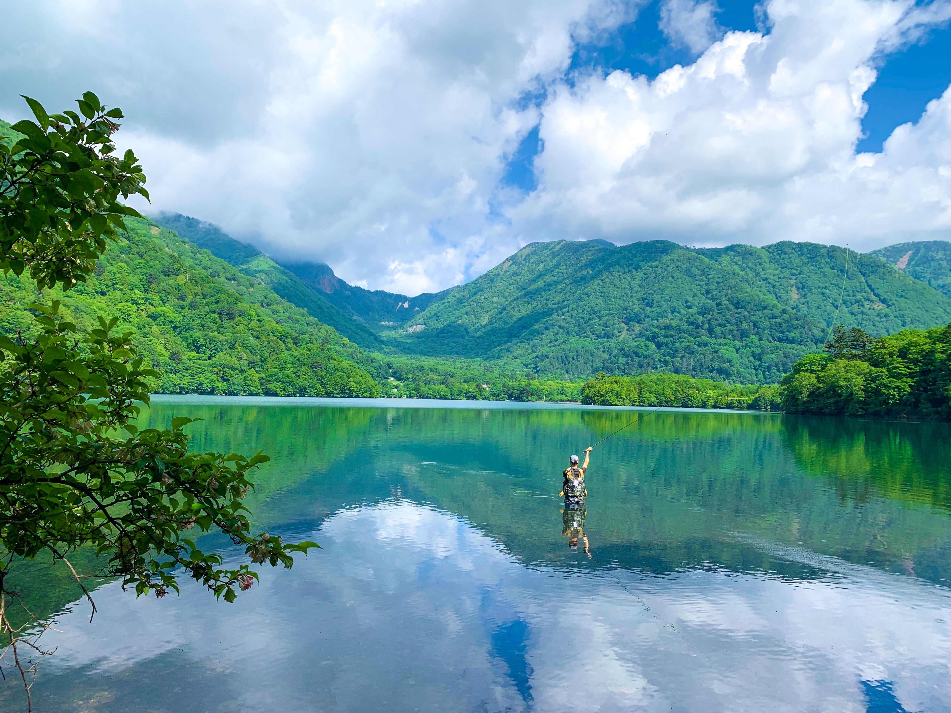 Um lago tranquilo rodeado por montanhas verdes e exuberantes sob um céu parcialmente nublado.