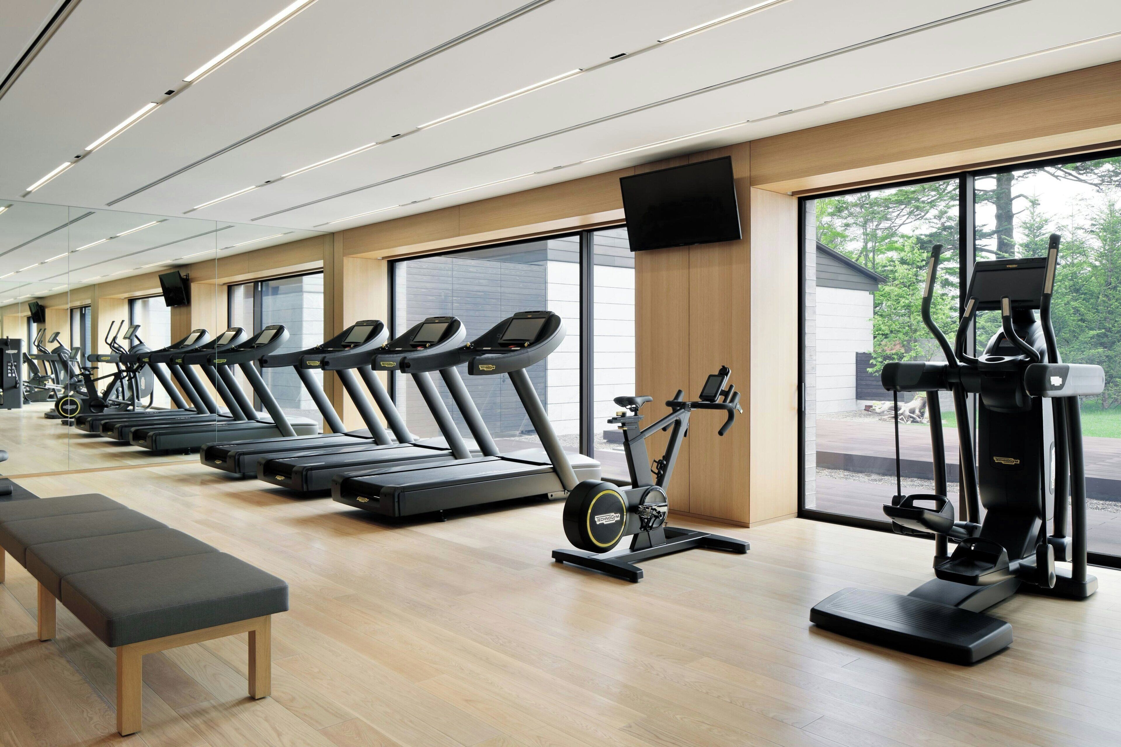 Un gimnasio con cintas de correr, una bicicleta estática y un banco.