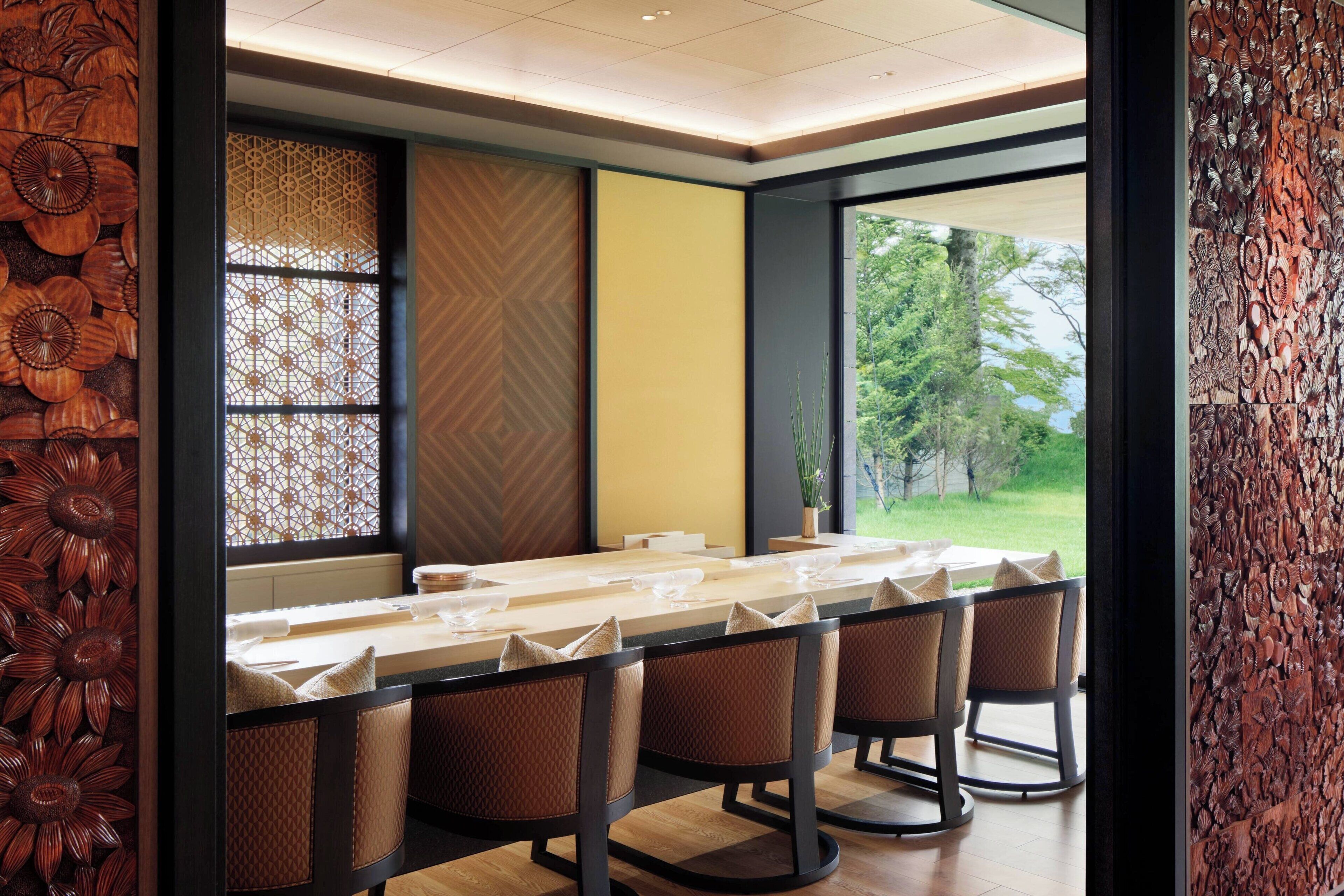 Een eethoek met een lange tafel, stoelen en uitzicht op groen.