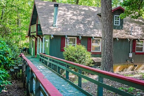 Traditional cabin with a steeply pitched roof and wooden deck, surrounded by lush greenery.
