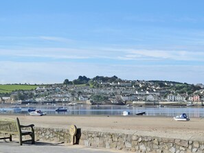 A coastal town with a stone wall, a bench, and boats on the water.