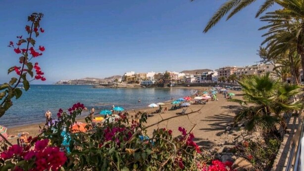 A beach with a clear view of the sea, a sandy shore, and buildings in the background. - GRAN CANARIA HOME (7), ARGUINEGUIN BEACH AND SUN (Arguineguin)
