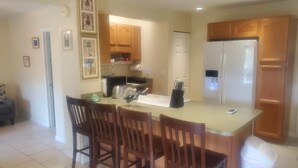 Una cocina con armarios de madera, un refrigerador, una mesa de comedor con sillas y un cubo de basura.