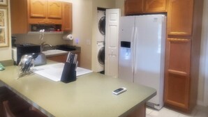 Cocina compacta con armarios de madera, un refrigerador, lavadora y encimera con teléfono y utensilios.