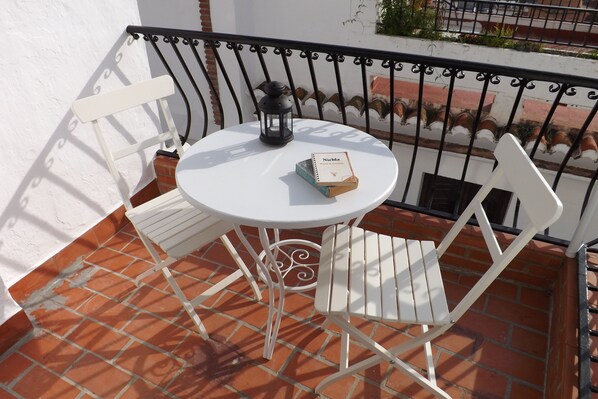 A white metal table with a black lantern and a book titled "Niebla" on a tiled patio with white metal chairs.