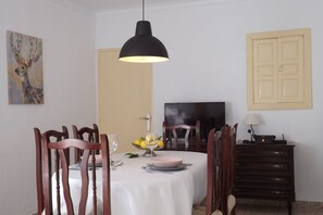 A dining area with a table set for two, a television, and a cabinet with drawers.