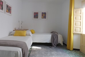 A room with two beds, a bedside table, a lamp, and artwork on the wall.