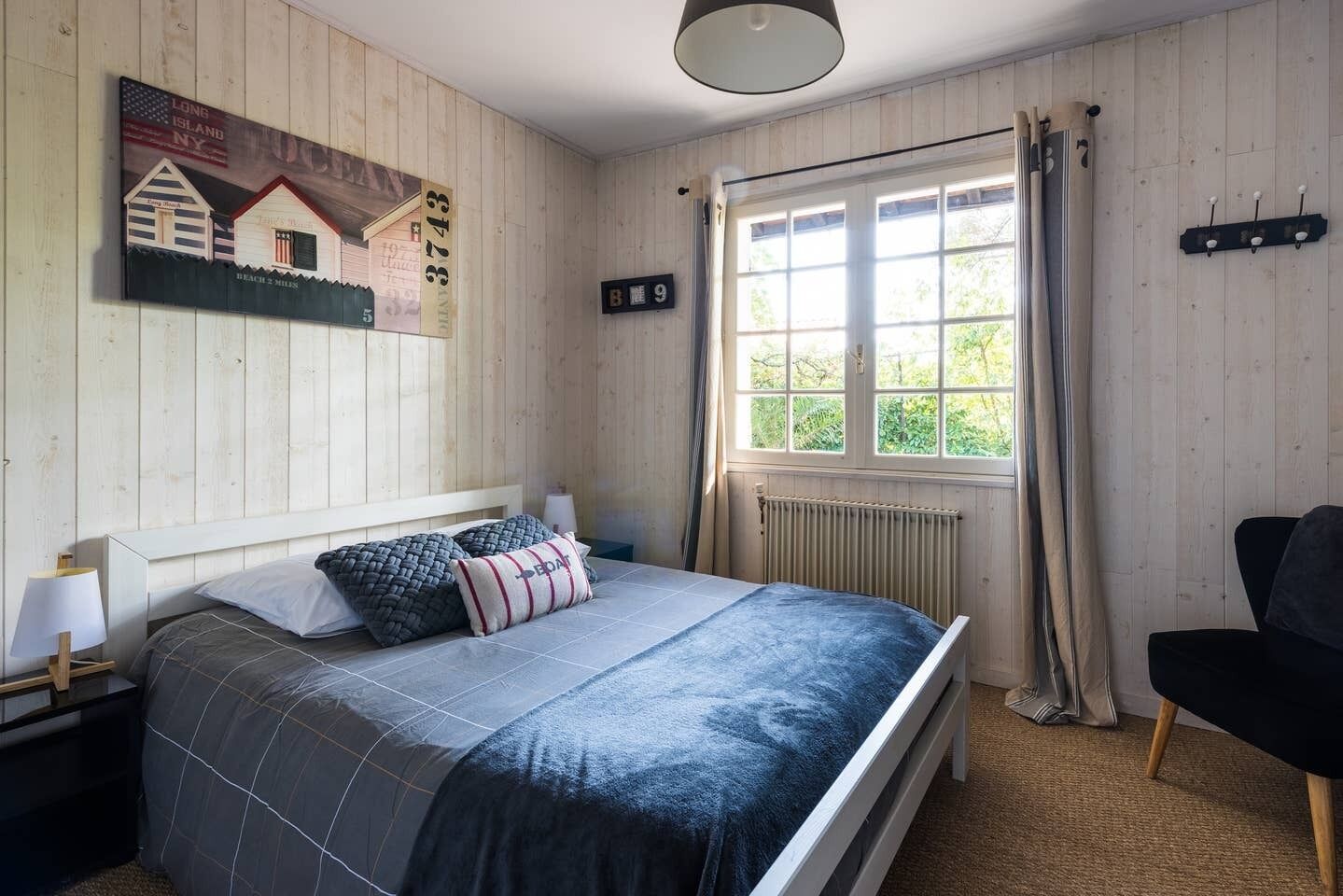 Ein Schlafzimmer mit Bett, Nachttisch, einem Fenster mit Vorhängen und einem an der Wand befestigten Schild.