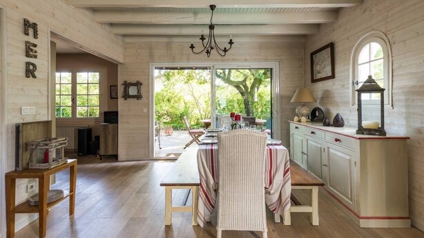Une cuisine rustique avec des poutres en bois, un lustre et une vue sur le jardin grâce à de grandes fenêtres.
