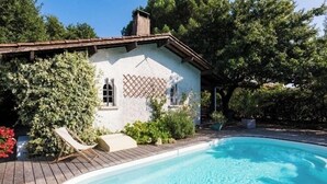 Une maison avec une piscine, entourée de verdure et dotée d’une terrasse en bois.