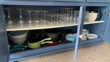 A kitchen with blue cabinets, a countertop, and various kitchenware including pots, pans, and wine glasses.