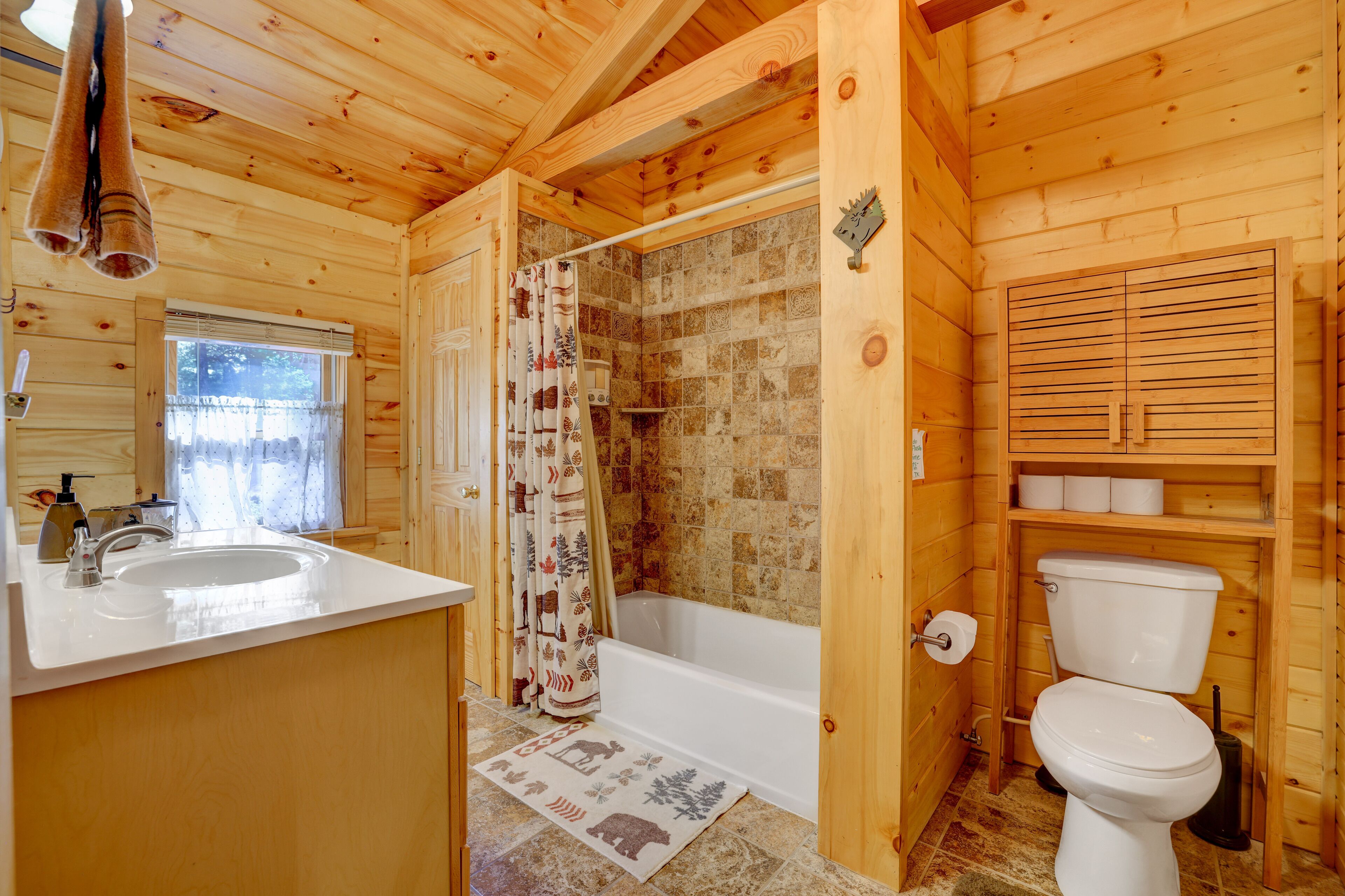 A wooden cabin bathroom with a bathtub, toilet, and sink.