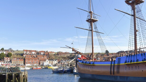 A tall ship docked at a harbor with a town in the background.