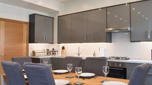 A modern kitchen with dark cabinets, a wooden dining table, and four grey upholstered chairs.