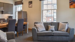 A modern living room with a grey sofa, a dining table, and a kitchen area with cabinets and appliances.