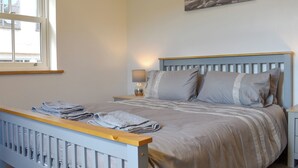 A bedroom with a bed, a nightstand, a lamp, a window with curtains, and a painting on the wall.