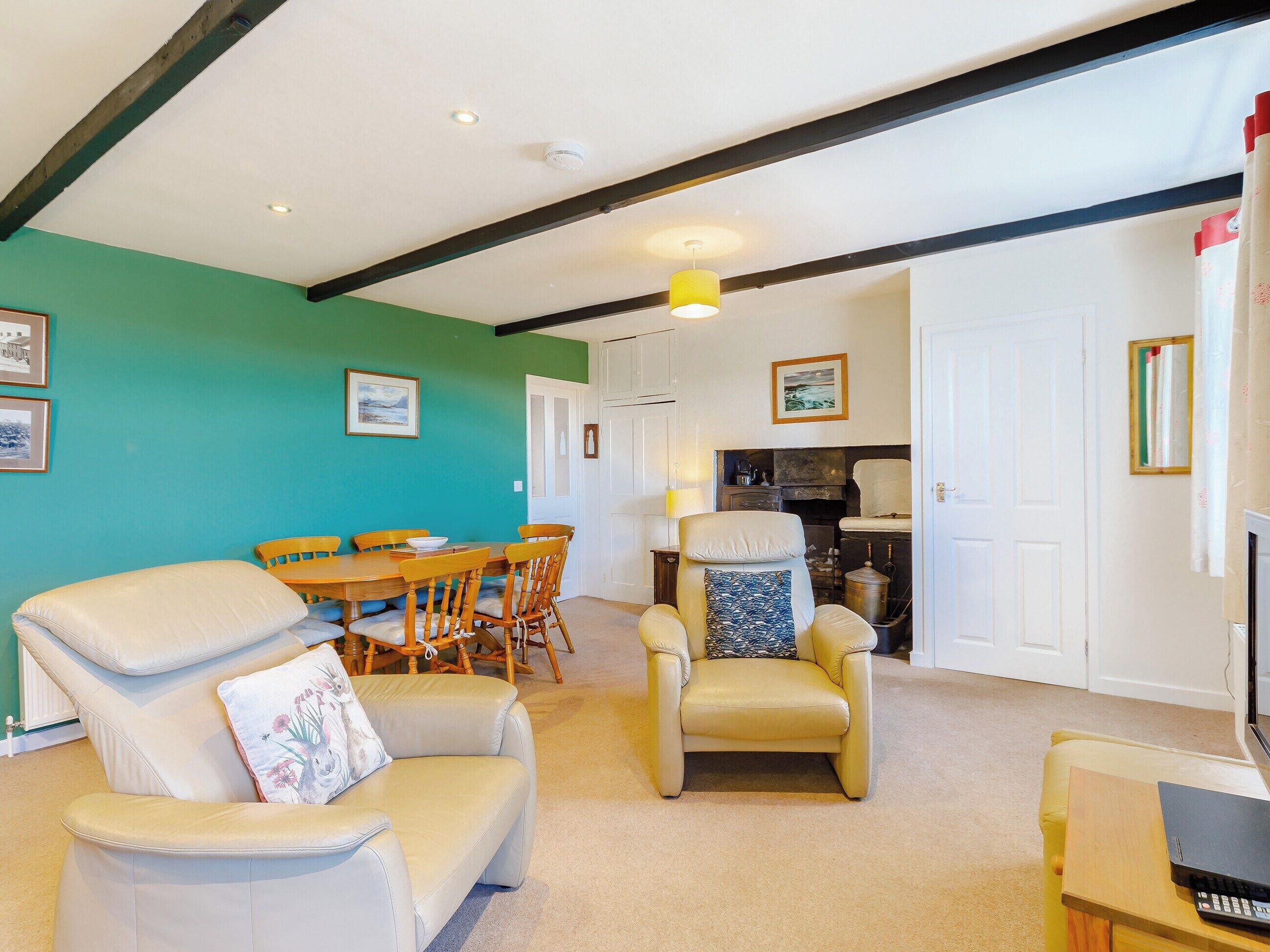 A living room with a teal wall, a dining area with wooden chairs, a beige sofa, and a yellow pendant light.
