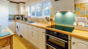 A modern kitchen with white cabinetry, a built-in microwave, a stainless steel oven, and a window with a view of trees.