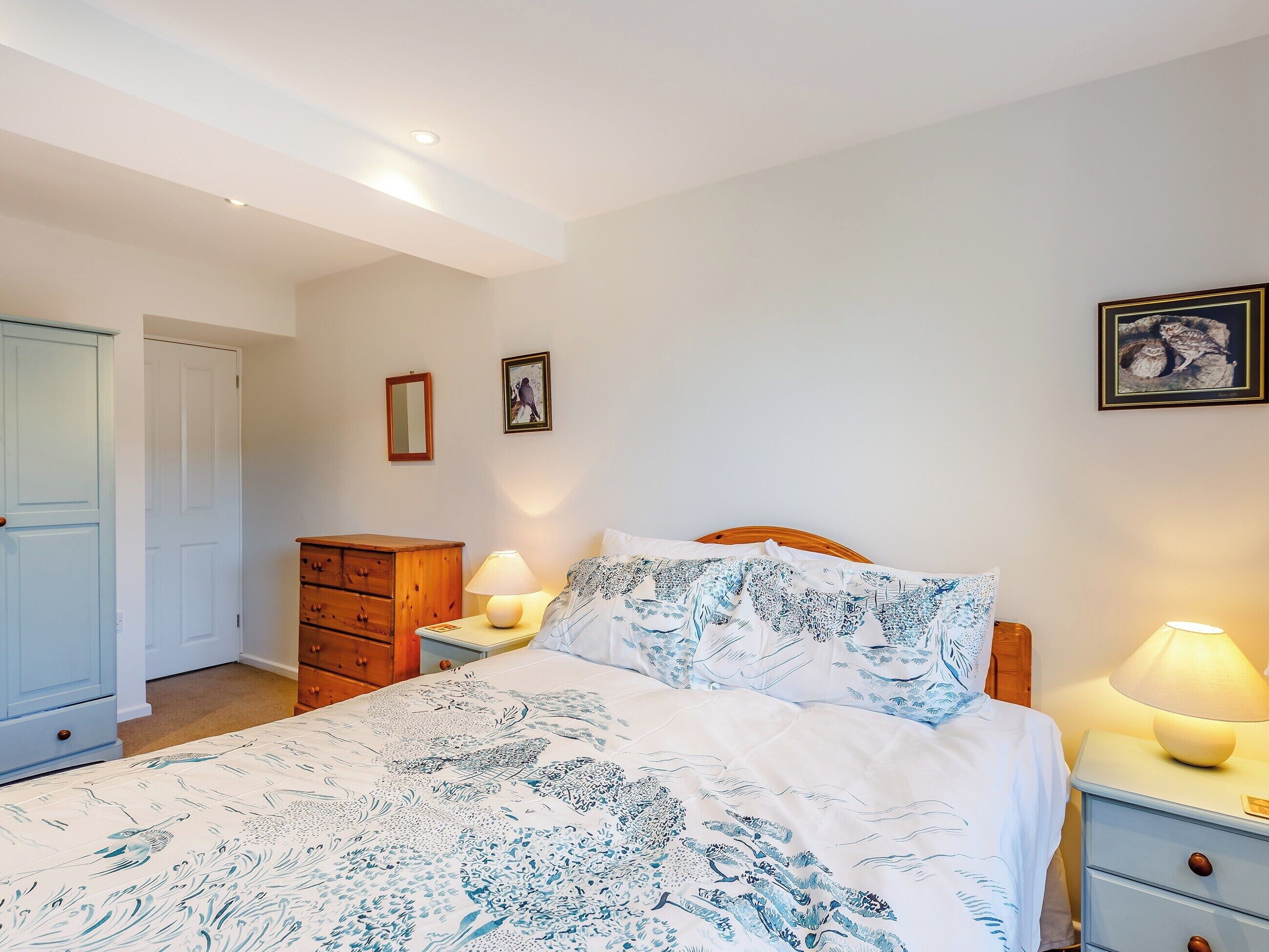 A bedroom with a bed, a dresser, a nightstand with a lamp, and a door.