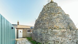 A stone structure adjacent to a house with a paved pathway leading to it.