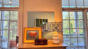 A room with a large window, a framed painting, a lamp, and a small table.