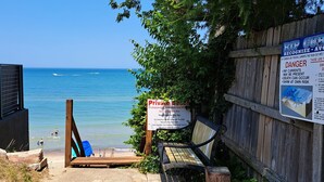 Ingresso spiaggia con recinzione in legno, cartello di avviso sulle correnti e una panchina.