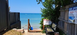 Una entrada a la playa con una cerca de madera, un letrero que advierte sobre corrientes de arrastre y un banco.